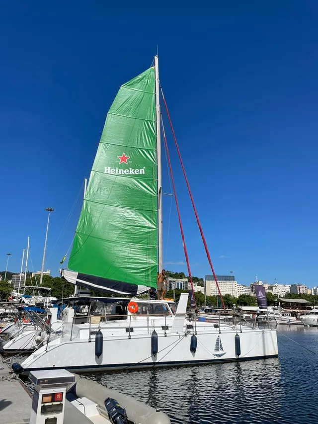 Veleiro com vela Heineken e identificação da marca, visto durante o dia.